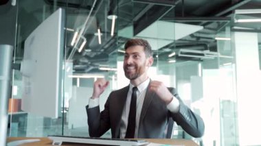 Masada oturan, modern bir ofiste çalışan yakışıklı, neşeli, genç bir iş adamı. Kafasına para saçıyor. Mutlu gülümseyen adam havaya para atıyor. Kazanan zafer, finansal büyüme başarısı