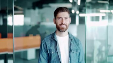 Sakallı, genç ve yakışıklı bir adamın portresi. Modern dünyada durup gülümseyen yaratıcı bir ofis çalışanı. Mutlu erkek çalışan, mimar ya da tasarımcı. İş yerinde gülümseyen kameraya bakıyorum.