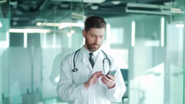 医生站在一家现代化的医院诊所里用的是手机 男医生利用智能手机治疗师的观点撰写相应的短信 阅读搜索信息新闻 有耐心的聊天 — 图库视频影像