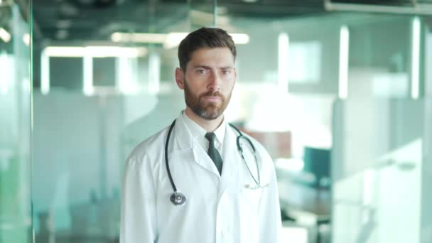 穿着白色长袍 站在现代医院诊所里 目不转睛地看着镜头的快乐快乐的男医生 — 图库视频影像