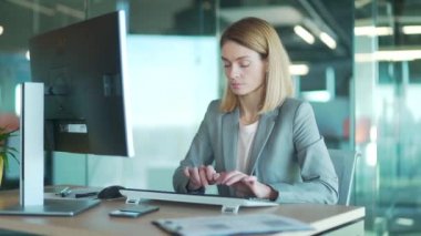 Bilgisayar bilgisayarında çalışan takım elbiseli kadın ofis çalışanı masada oturan monitör yazışmalarının önünde oturuyor. Modern bir işyerinde çalışan. Sarışın kadın meşgul girişimci sekreter kısa mesaj yazıyor.
