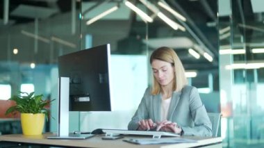 Bilgisayar bilgisayarında çalışan takım elbiseli kadın ofis çalışanı masada oturan monitör yazışmalarının önünde oturuyor. Modern bir işyerinde çalışan. Sarışın kadın meşgul girişimci sekreter kısa mesaj yazıyor.