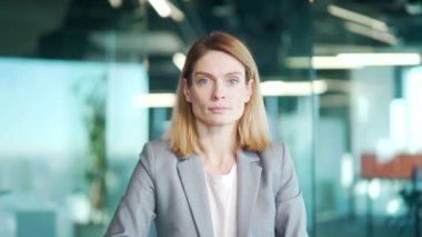 Modern ofis arka planında kameraya bakarak kendine güvenen bir iş kadınının yakın portresi. İç mekan. Beyaz, olgun, sarışın kadın çalışan ya da girişimci. İş yerindeki ofis çalışanı.
