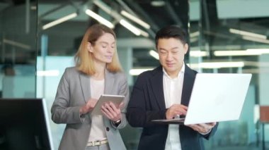 Dijital tablet üzerinde çalışırken konuşan iki Asyalı erkek ve kadın meslektaşımız laptopta projeyi tartışıyorlar. Mutlu çalışanlar, işçiler birlikte iletişim kurar. gülümsüyor