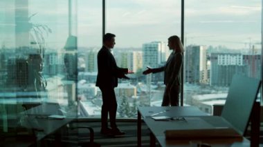 Modern ofis odasında iş ortaklarıyla tanışma silueti pencere arkasında duruyor. Kapalı alanda. Asyalı adam bir kadınla tokalaşıyor. İki işadamı müzakere hakkında konuşuyor.