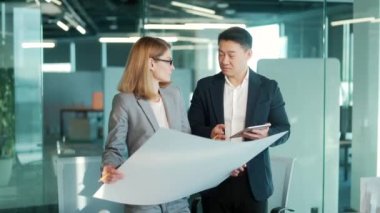 Grup genç yaratıcı mühendisleri modern ofiste yeni projeyi tartışıyorlar bir plan okuyorlar. Takım düşünceli mimar tasarımcısı. Dijital tablet kullanan Asyalı erkek ve kadın meslektaşlar