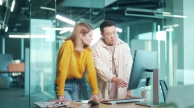 Yaratıcı insanlardan oluşan günlük giysi takımındaki iki genç meslektaşımız modern ofiste çalışırken ekrandaki konuşmalara işaret ederek bilgisayar üzerinden projeyi tartışıyor.