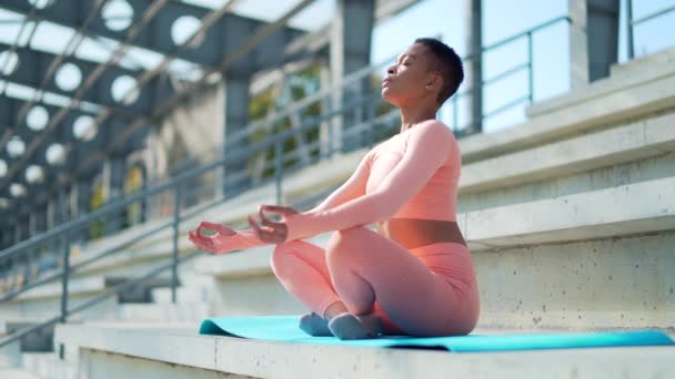 非洲裔美国妇女在体育馆附近的公园里 坐在瑜伽垫上进行呼吸练习 训练后休息 黑色女性在荷花的位置上沉思和放松 — 图库视频影像