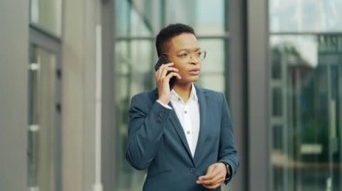 Ciddi bir Afro-Amerikan iş kadını cep telefonuyla konuşuyor. Siyahi girişimci kadın çalışanlar dışarıda iletişim kuruyor. Gözlüklü ofis çalışanı konuşuyor. Resmi takım elbiseli iş kadını Dönüşümü