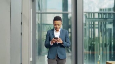 Şehir merkezinde yürüyen siyahi iş kadını. Cep telefonunu kullan ve bak. Afrika kökenli Amerikalı kadın girişimci şehir geçmişinde akıllı telefon okudu. kendine güvenen ofis çalışanı