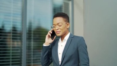 Mutlu Afro-Amerikan kadın girişimci şehir caddesinde modern bir ofisin yanında cep telefonuyla konuşuyor. Siyahi kadın konuşuyor, anlatıyor, şehir dışında bir cep telefonuyla iletişim kuruyor.