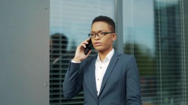 Ciddi bir Afro-Amerikan iş kadını cep telefonuyla konuşuyor. Siyahi girişimci kadın çalışanlar dışarıda iletişim kuruyor. Gözlüklü ofis çalışanı konuşuyor. Resmi takım elbiseli iş kadını Dönüşümü