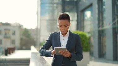 Afro-Amerikan iş kadını resmi takım elbiseli bir çalışan dışarıda arka plandaki modern ofis binasında tabletle çalışıyor. Şehir dışında akıllı telefon ya da cep telefonu kullanan bir kadın.