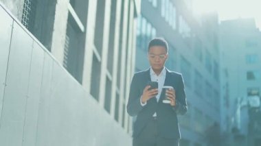 Kendine güvenen başarılı genç iş kadını cep telefonuyla modern ofis binasına karşı hareket ediyor şehir merkezindeki iş kadını elinde bir kahve fincanıyla cep telefonu akıllı telefonu kullanıyor.