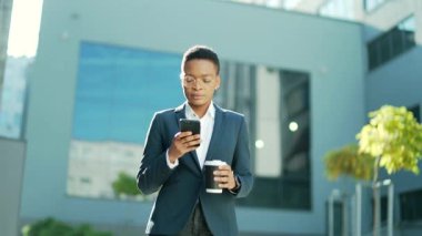 Kendine güvenen başarılı genç iş kadını cep telefonuyla modern ofis binasına karşı hareket ediyor şehir merkezindeki iş kadını elinde bir kahve fincanıyla cep telefonu akıllı telefonu kullanıyor.