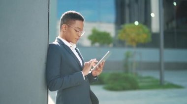 Afrikalı Amerikalı kadın üniversite ya da üniversite öğrencisi kampüste duruyor ve dijital tablet kullanıyor. Siyah genç kız internette cep telefonuna bakıyor, akıllı telefon. Dışarıdaki ofis çalışanı ya da çalışanı.