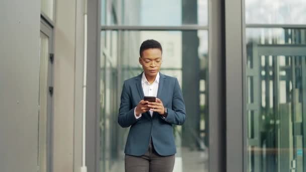 ダウンタウンの街を歩く黒人女性は携帯電話を見て使います アフリカ系アメリカ人女性従業員起業家は 都市部の背景にスマートフォンを読む 自信のあるサラリーマン — ストック動画