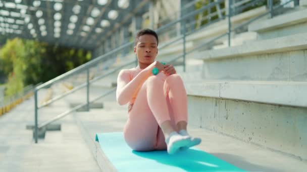 運動アフリカ系アメリカ人の運動選手がマットの上で持久力の練習をしている 屋外だ 黒の女性は外の近代的な都市のスタジアムで列車 フィットネス体操 新鮮な空気の中で — ストック動画