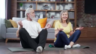 Üst sınıf çifti evde yoga yapıyor. Kapalı alanda. Yetişkin bir aile oturma odasında yoga minderinde nefes egzersizi yapıyor. Meditasyon yap ve gözlerin kapalı rahatla. Lotus Pozu 'nda sakinleş. Emeklilik