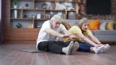 Aktif olgun yaşlı çift gerinme egzersizi yapıyor ve evde yoga yapıyor. Pilates, fitness ya da jimnastik yaparken mutlu, kır saçlı bir aile. Sağlıklı Yaşam Tarzı