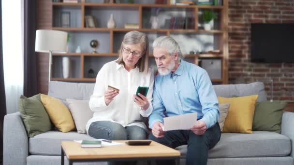 年长的家庭夫妇 灰发老人的工资 服务输入数据文件使用应用程序移动智能手机信用卡 退休的老年人在家里 公用设施账单 支票使用电脑智能电话 — 图库视频影像