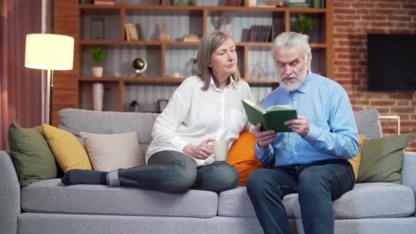Para Seniorów Spędza Wolny Czas Czytając Razem Książkę Siedząc Wygodnej — Wideo stockowe