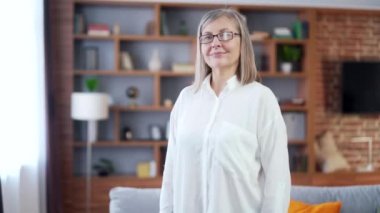 Kameraya bakıp gülümseyen yaşlı, gri saçlı bir kadının portresi. İç mekan. Modern bir evde ya da ofiste. Kollarını kavuşturan güzel, mutlu, yaşlı bir iş kadınının yüzünü kapat. Memnun, kendine güvenen emekli.