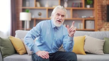 Kendinden emin ve deneyimli beyaz saçlı adam kameraya bakarak konuşuyor. Görüntülü arama ile iletişim kuruyor. Web kamerası görüntüsü. Olgun erkeği günlük tişört kayıt videosuyla açıklıyor. İnternetten yayınlanıyor.