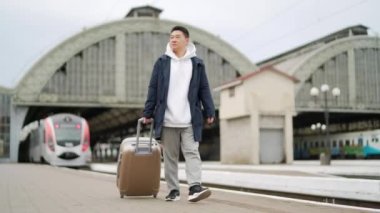 Asyalı yolcu büyük bir bavulla şehre gelir ya da trenle gider. Tren istasyonundaki turist platforma çıkar. Gezgin şehre varır.