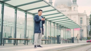 Otobüste ya da tren durağında telefon kullanan Asyalı bir adam. Asyalılar otobüs durağı için akıllı telefon kullanırlar, telefonla taksi çağırırlar, iş seyahatleri için internet üzerinden yer ayırtırlar.