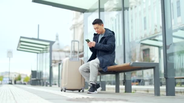 在公共汽车站的游客 用手机预订出租车 亚洲男性在线预订住宿 供公务旅行用的现代火车在城市的公共交通 — 图库视频影像