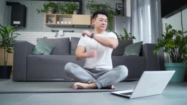Happy Asian evde yoga yapıyor, lotus pozisyonunda oturuyor, adam online dersler için dizüstü bilgisayar kullanıyor, aktif bir yaşam tarzı uyguluyor. dizüstü bilgisayar öğrenme derslerini izle