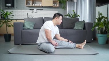 Asyalı bir adam sabah jimnastiği ve spor egzersizlerini evde oturma odasındaki paspasın üzerinde yapıyor. Aktif atletik erkek karın egzersizi, içerde yoga yapmak ve egzersiz yapmak.