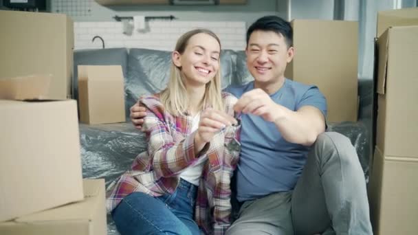 肖像画自豪的年轻主人夫妇拿着钥匙站在自己的新公寓里 笑亚洲人的丈夫和妻子 家人在镜头前看到一个新家 抵押贷款投资概念 — 图库视频影像