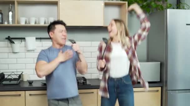 这对欢快有趣的夫妇在厨房里跳舞唱歌 亚洲男人和女人在家里跳舞 年轻的家庭一起度过时光 庆祝搬家去新家的日子 快乐的妻子和丈夫一起做饭 — 图库视频影像