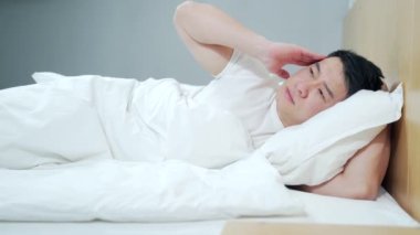 Genç Asyalı adam evde depresyondayken yatakta üzgün yatıyor. Kötü hissettiriyor. Mutsuz, bitkin, düşünceli ve düşünceli bir erkek. Üzüntüden acı çekerken düşüncelere dalmak duygusal baş ağrısı