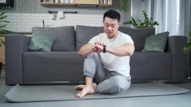 Spor adam evde fitness akıllı saati kullanıyor. Genç erkek daha önce egzersiz yaparken akıllı saat eğitim veri uygulamasını izliyor. Antrenmandan sonra kalp atışları, nabız ve giyilebilir uygulamalar gözlemleniyor.