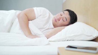 Mutsuz Asyalı adam sabah uyanmak istemiyor. Cep telefonu akıllı telefonundaki çalar saati kapatır. Geç oldu. Kalkma vakti. Yatakta uyuyakalan yorgun ve sinirli genç bir erkek.