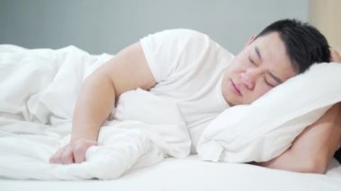 Genç Asyalı adam evde depresyondayken yatakta üzgün yatıyor. Kötü hissettiriyor. Mutsuz, bitkin, düşünceli ve düşünceli bir erkek. Üzüntüden acı çekerek acı çekmeyi düşünmek, depresyona girmek.