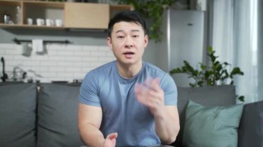 Günlük kıyafetli genç Asyalı bir adam kameraya bakarken konferans toplantısı, danışma ya da tavsiye dinliyor. Odada uzaktan görüntülü arama yapan bir erkek var. Web kamerası görünümü portresi