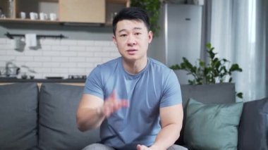 Günlük kıyafetler içinde Asyalı bir genç internetten konuşuyor, uzaktan görüşme ya da konferans, web kamerası görüntülerini öğreniyor. Evdeki konuşmada elini sallayan kameraya bakan erkek portresi. İç mekan