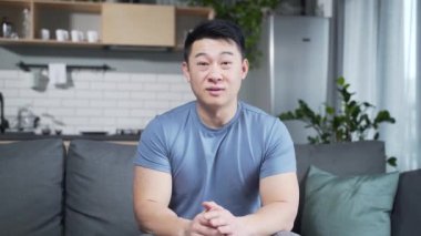 Günlük kıyafetler içinde Asyalı bir genç internetten konuşuyor, uzaktan görüşme ya da konferans, web kamerası görüntülerini öğreniyor. Evdeki konuşmada elini sallayan kameraya bakan erkek portresi. İç mekan