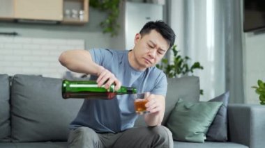Evde kederli bir şekilde içki içen sarhoş Asyalı adam. Depresyon, mutsuz hüsran, alkol istismarı, bağımlılık, belirlenmiş insanlar konsepti. Stresli erkek, alkolik, kanepede oturuyor. 