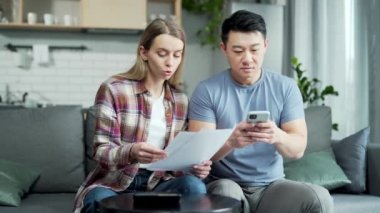 Genç bir çift online bankacılık uygulamasını telefonla kullanıyor. Verilere ulaşmak için para ödeyen erkek ve kadın evdeki uygulama cep telefonunu kullanıyor. Faturalar, çekler bilgisayar akıllı telefonu kullanıyor