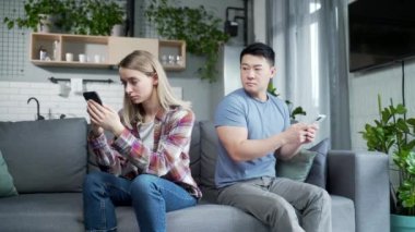 Genç, çok ırklı bir aile, odadaki koltukta oturan kavgacı bir adam ve kadın, farklı yönlere döndüler. Çift arka arkaya akıllı telefonları kullanarak sosyal ağda sohbet ediyor.