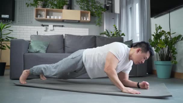 亚洲男人在家里 做健身和运动 在家里客厅里 从地板上推下来 运动男性在室内垫子上做运动酒吧俯卧撑 — 图库视频影像