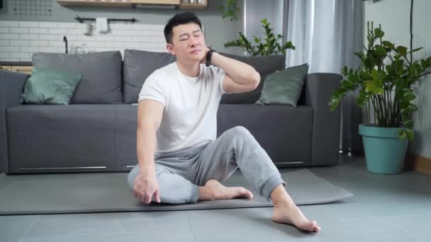 若いアジアの男性の練習家の屋内で背の筋肉を伸ばす 運動能力男性は 肩の首や関節の筋肉のけいれんで痛みを被る ヨガマットに座ってトレーニングした後の緊張 — ストック動画