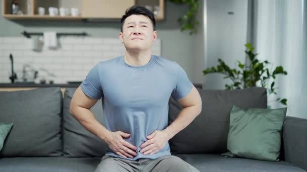 ソファの上で自宅に座っている間 アジアの男は腹部の痛みに苦しんでいます 胃の痛み 下痢胃炎問題胸焼け重度の胃痙攣 — ストック動画