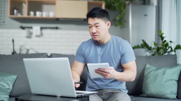 年轻的亚裔男子通过在线课程在家里上大学 远距离教育 男子使用笔记本电脑进行远程学习询问有关视频咨询的建议 并在笔记本上书写 — 图库视频影像