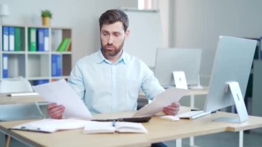 Bir erkek çalışanın evrak işleriyle uğraşması zor. Belgeler. Stresli Kafkasyalı işadamı yanlışlıkla kafasını karıştırmış, evraklara bakıyor. Muhasebeci, muhasebeci belli belirsiz, ofiste loş bir şekilde oturuyor.